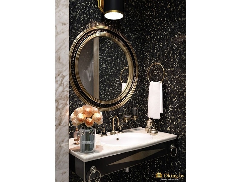 стена под зеркалом оформлена черной плиткойс рисунком мраморной крошки, зеркало круглое, рама и смесители бронзовые в ретро-стиле